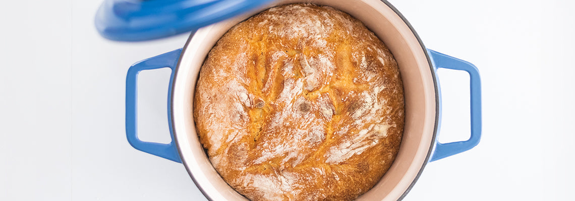 A bird’s eye view of a freshly baked loaf of bread inside a blue Misen Dutch Oven, with the lid — which is off — slightly visible.
