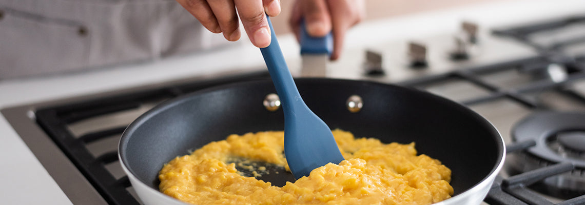A hand uses a Misen Spatula to stir scrambled eggs in a Misen Nonstick Pan on a stovetop.