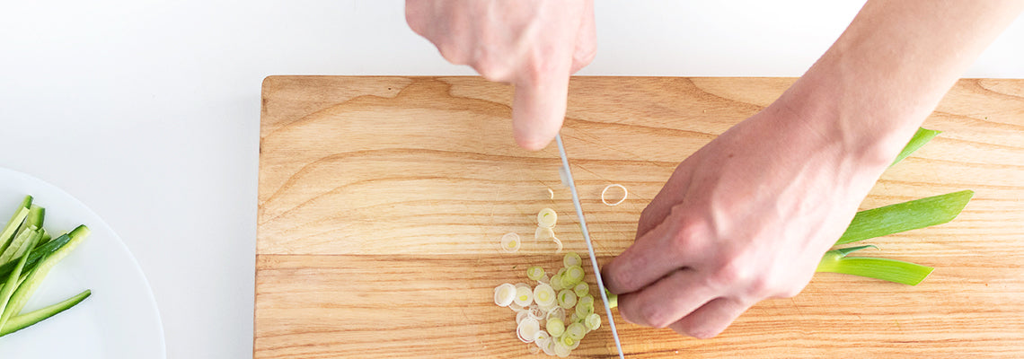 A bird’s eye view of a chef finely chopping scallions with a Misen Knife on a wood Misen cutting board.