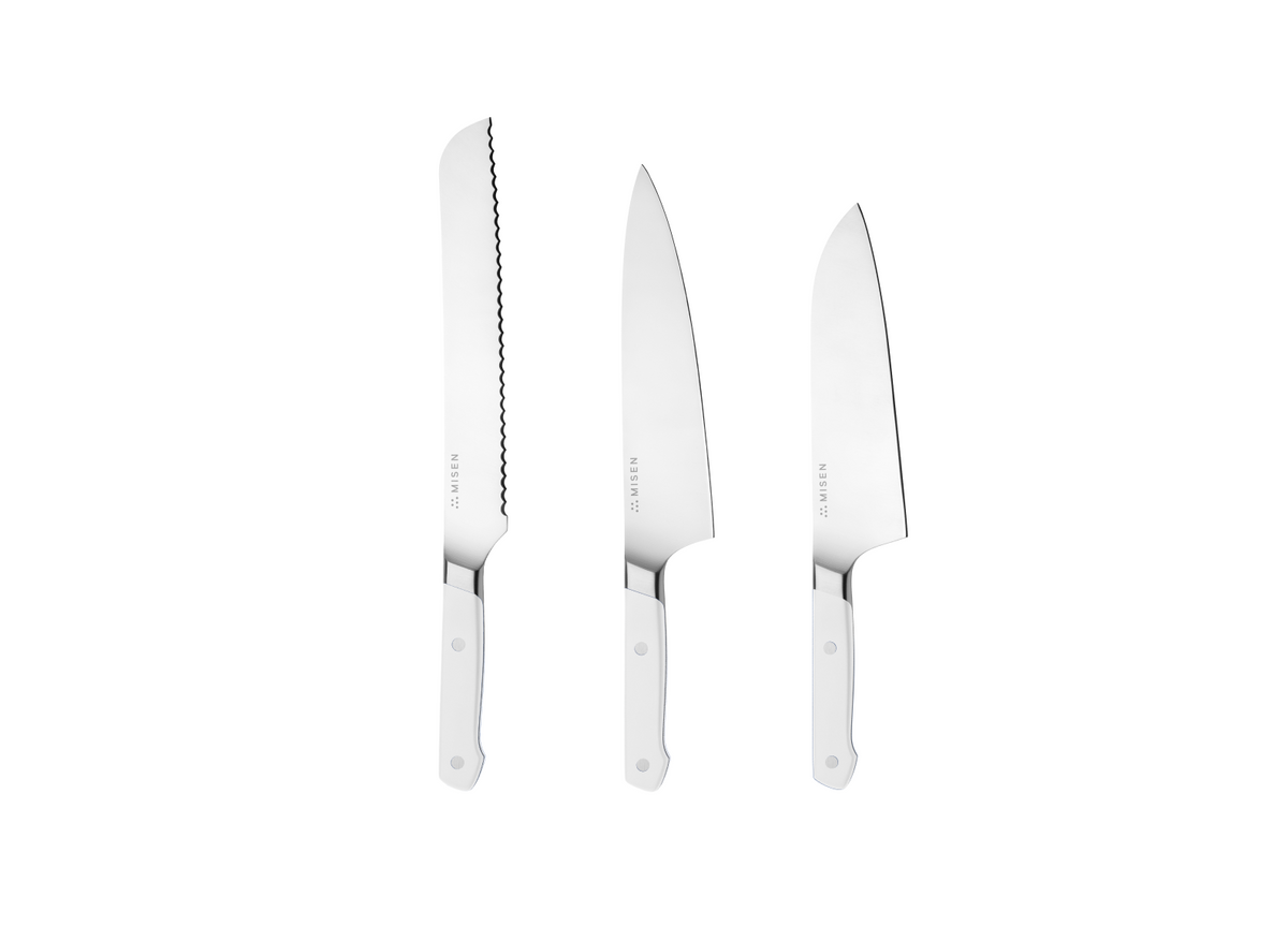 Three stainless-steel knives with white handles: long serrated blade, large chef's blade, shorter straight, stamped MISEN.