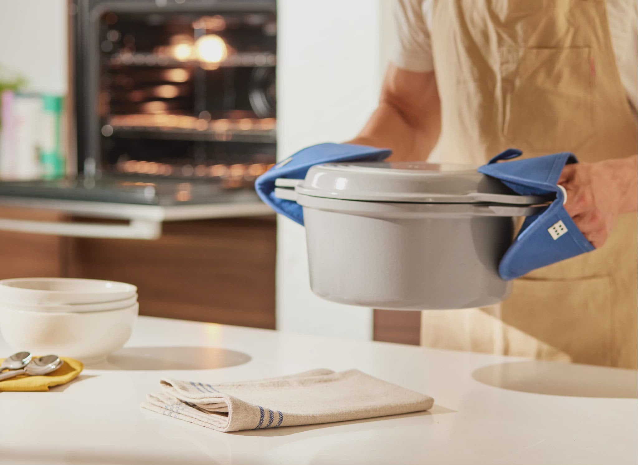 A GIF shows a chef using two Misen Pot Holders to set a gray Misen Dutch Oven down on a white dishtowel on a countertop. 