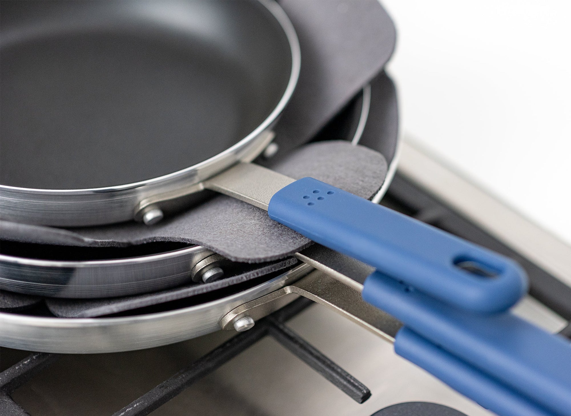 {{1-pack,2-pack}} Stack of three Misen Nonstick Pans on a stovetop with two grey felt pan protectors visible between them.