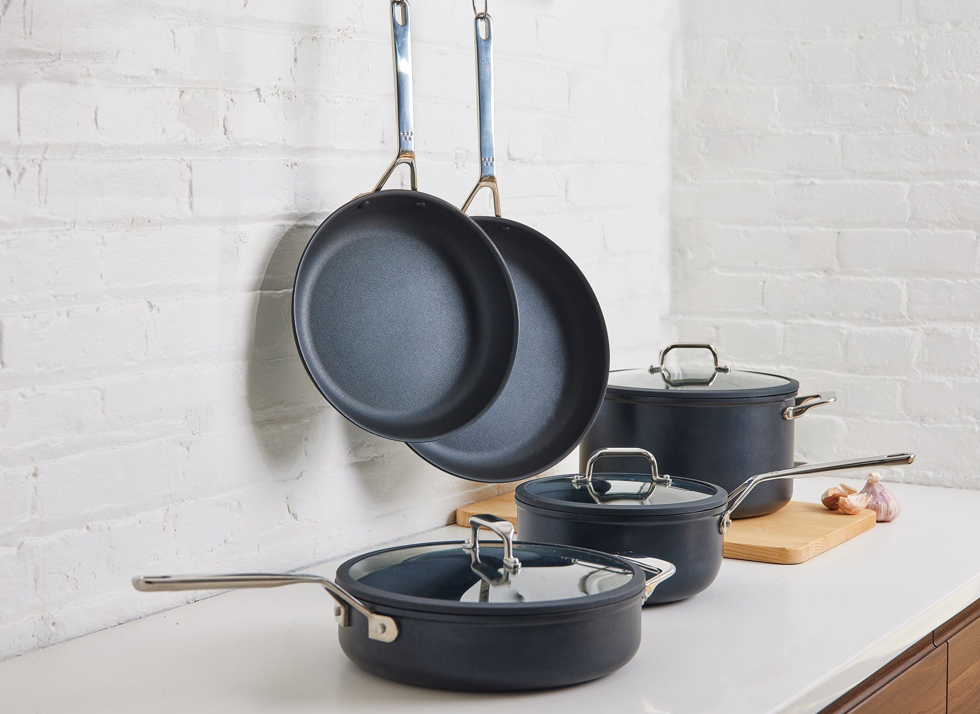 The Misen 9-Piece Essentials Cookware Set on kitchen counter, with most pieces visible: the 10- and 12-inch Nonstick Pans hanging from hooks, the Nonstick Stock Pot, Nonstick Sauté, and Nonstick Saucier, with lids.