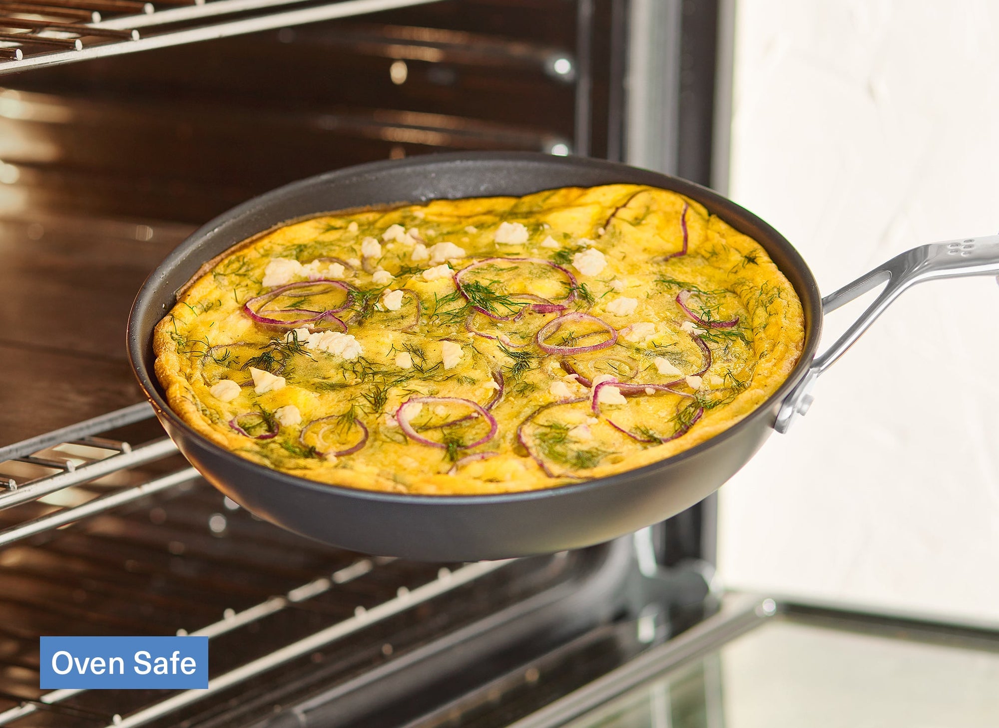 A Misen Nonstick Pan is being pulled out of an oven. Inside is a frittata with onions, herbs, and cheese. A caption reads “Oven Safe”