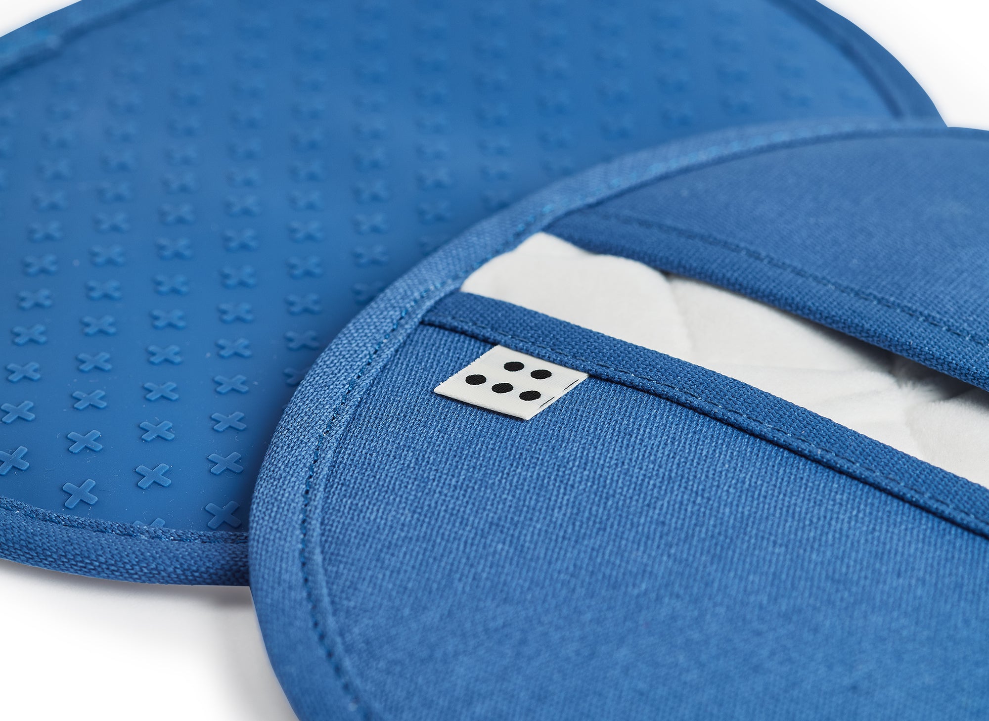 A close up shot of two Misen Pot Holders in blue. The gripped side of one pot holder is visible, as is the opening of the other pot holder, with the Misen logo on a tag. 