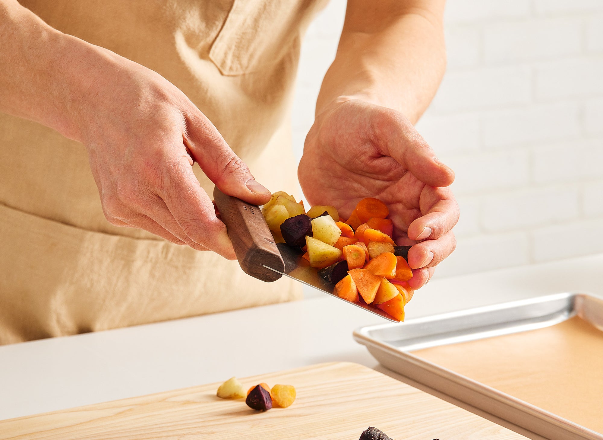 {{walnut,blue}} A pair of hands uses a Misen Bench Scraper with walnut handle to scoop chopped root vegetables up from a Misen Wood Cutting Board.