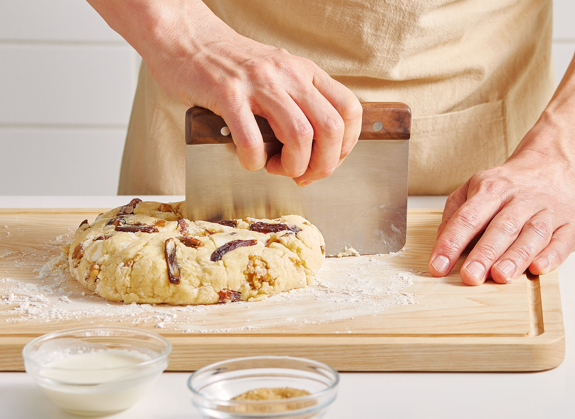 {{walnut,blue}} A pair of hands uses a Misen Bench Scraper with walnut handle to divide scone dough into even sections, working atop a Misen Wood Cutting Board.