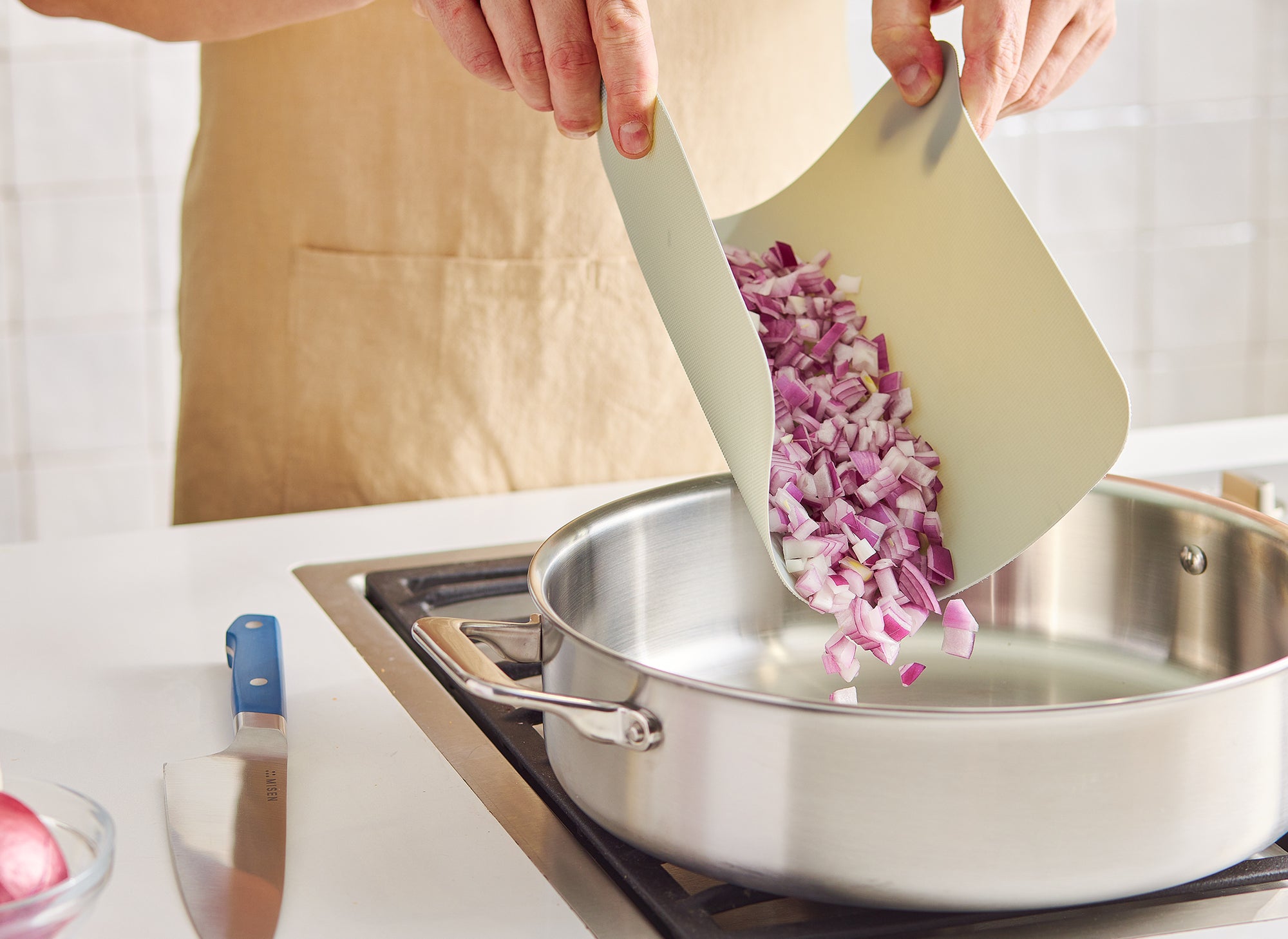 {{plastic}} A chef folds a small Misen Cutting Sheet in order to pour diced red onion into a Misen Rondeau for cooking.