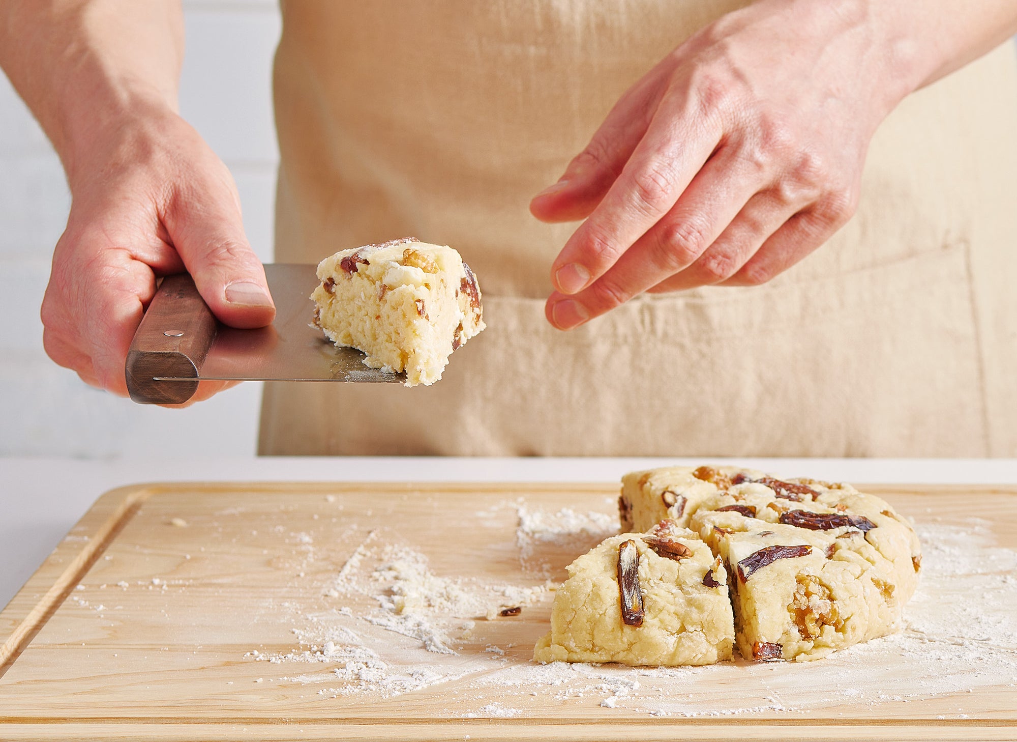 {{walnut,blue}} A pair of hands holds a Misen Bench Scraper with walnut handle and a piece of dough, as they divide scone dough into sections, working atop a Misen Wood Cutting Board.