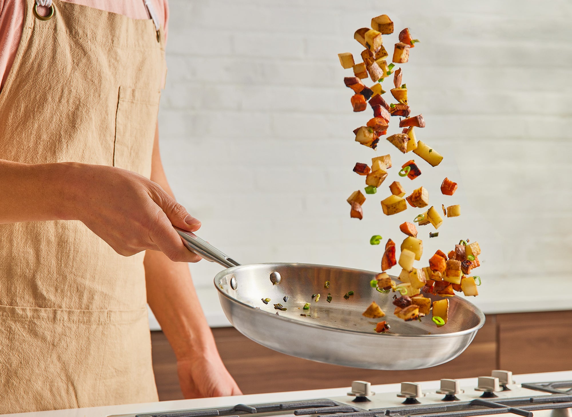 A chef uses a Misen Stainless Steel Pan to toss roasted root vegetables over a stovetop.