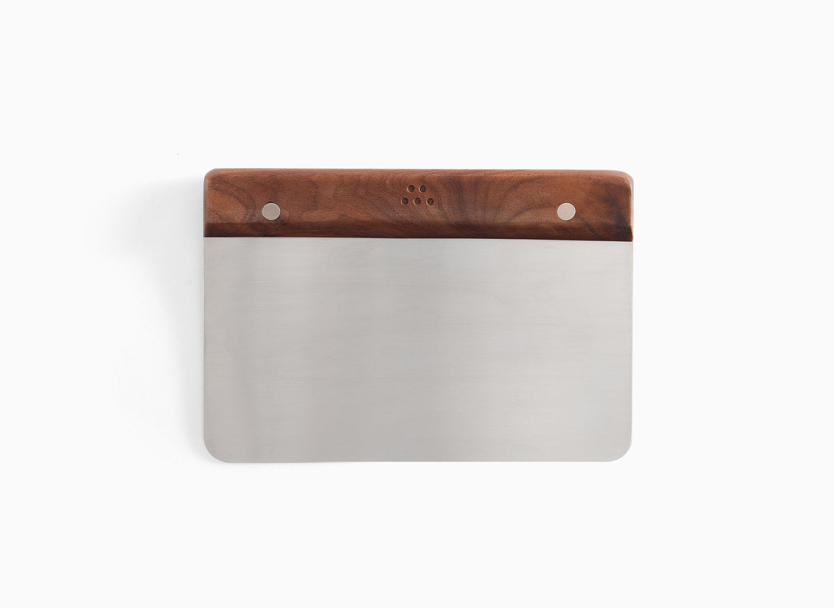 A front-facing view of the Misen Bench Scraper with walnut handle on a white background, with the handle facing upward and full view of the blade. 
