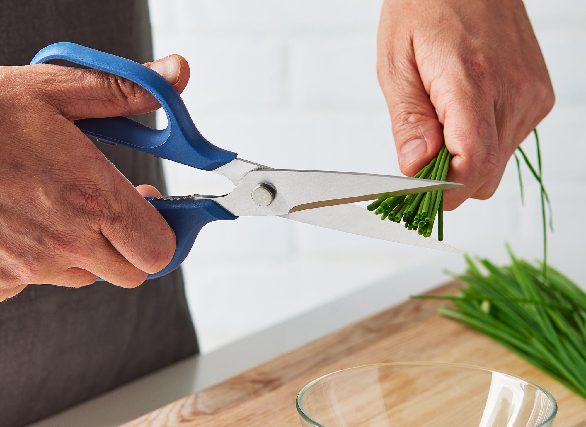{{blue,black,gray,green,red}} A chef using Blue Misen Kitchen Shears to cut a bundle of chives over a glass bowl.